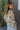 Side view of model wearing the First Love Floral Top, that has teal fabric with a metallic gold and ivory floral print, a surplice neckline, flowy balloon sleeves with smocked cuffs, and an elastic waist