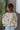Back view of model wearing the First Love Floral Top, that has teal fabric with a metallic gold and ivory floral print, a surplice neckline, flowy balloon sleeves with smocked cuffs, and an elastic waist