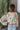 Back view of model wearing the First Love Floral Top, that has teal fabric with a metallic gold and ivory floral print, a surplice neckline, flowy balloon sleeves with smocked cuffs, and an elastic waist