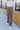 Front view of model wearing the Don't Wait Up Pants, that have brown woven fabric with front pleating, a front zipper and hook closure, side pockets, and faux back pockets