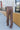 Back view of model wearing the Don't Wait Up Pants, that have brown woven fabric with front pleating, a front zipper and hook closure, side pockets, and faux back pockets