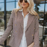 Front view of model wearing the Better This Way Houndstooth Blazer, that features a brown houndstooth pattern, gold buttons, lapels, and a pocket on each side. Worn over white shirt.