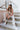 Front view of model wearing the At Your Leisure Pants, which feature ribbed knit beige fabric and an elastic waist. Model is sitting on stairs.