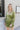 Front view of model wearing the Supernova Velvet Romper in Green, which has light green crushed velvet, a surplice neckline, a front skirt overlay with a side tie, and long fitted sleeves