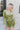 Front view of model wearing the Supernova Velvet Romper in Green, which has light green crushed velvet, a surplice neckline, a front skirt overlay with a side tie, and long fitted sleeves