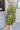 Side view of model wearing the Supernova Velvet Romper in Green, which has light green crushed velvet, a surplice neckline, a front skirt overlay with a side tie, and long fitted sleeves