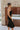 Side view of model wearing the Walk of Fame Midi Dress, which features patterned black velvet, black feathers across the neckline, adjustable thin straps, and a midi mermaid silhouette