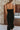 Back view of model wearing the Walk of Fame Midi Dress, which features patterned black velvet, black feathers across the neckline, adjustable thin straps, and a midi mermaid silhouette