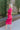 Side view of model wearing the New Look Midi Dress, that has pink satin fabric with a ruched midi-length skirt, a v-neckline, 3/4 length sleeves with ruching at the wrist, a back zipper and hook closure with a keyhole cutout