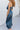 Side view of model wearing the Athena Midi Dress, that has blue satin fabric, a one-shoulder neckline with a braided back strap, a back cutout, and an asymmetrical midi hem.