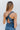 Close-up back view of model wearing the Athena Midi Dress, that has blue satin fabric, a one-shoulder neckline with a braided back strap, a back cutout, and an asymmetrical midi hem.