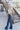 Full body side view of model wearing the Walk The Line Velvet Pants, which feature blue velvet with vertical and diagonal ribbed panels, flared legs, and a high-rise elastic waist.