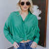 Front view of model wearing the Must Be True Top, which features green fabric, a button-up front with a tucked twist detail, long sleeves, and a collared neckline.