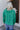Back view of model wearing the Must Be True Top, which features green fabric, a button-up front with a tucked twist detail, long sleeves, and a collared neckline.