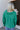 Back view of model wearing the Must Be True Top, which features green fabric, a button-up front with a tucked twist detail, long sleeves, and a collared neckline.