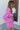 Side view of model wearing the Looking At You Romper, which features textured magenta fabric, a surplice neckline, a tie belt, and long bell sleeves.