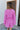Back view of model wearing the Looking At You Romper, which features textured magenta fabric, a surplice neckline, a tie belt, and long bell sleeves.