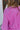 Close-up upper back view of model wearing the Looking At You Romper, which features textured magenta fabric, a surplice neckline, a tie belt, and long bell sleeves.