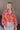 Front view of model wearing the Maui Dreaming Top, which features orange fabric with a pink floral print, long balloon sleeves, and a collared neckline. Shirt is tucked into skirt.