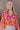 Front view of model wearing the Maui Dreaming Top, which features orange fabric with a pink floral print, long balloon sleeves, and a collared neckline. Shirt is tucked into skirt.