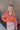 Front view of model wearing the Maui Dreaming Top, which features orange fabric with a pink floral print, long balloon sleeves, and a collared neckline. Shirt is tucked into skirt.