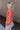 Side view of model wearing the Maui Dreaming Top, which features orange fabric with a pink floral print, long balloon sleeves, and a collared neckline. Shirt is tucked into skirt.