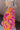 Close-up side view of model wearing the Maui Dreaming Top, which features orange fabric with a pink floral print, long balloon sleeves, and a collared neckline. Shirt is tucked into skirt.