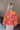 Back view of model wearing the Maui Dreaming Top, which features orange fabric with a pink floral print, long balloon sleeves, and a collared neckline. Shirt is tucked into skirt.