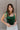 Front view of model wearing the Luna Velvet Bodysuit in Green, which features velvet fabric, satin tie straps, and a cheeky bottom. Worn with jeans.
