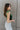 Side view of model wearing the Luna Velvet Bodysuit in Green, which features velvet fabric, satin tie straps, and a cheeky bottom. Worn with jeans.