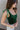 Frontal side view of model wearing the Luna Velvet Bodysuit in Green, which features velvet fabric, satin tie straps, and a cheeky bottom. Worn with jeans.