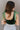 Back view of model wearing the Luna Velvet Bodysuit in Green, which features velvet fabric, satin tie straps, and a cheeky bottom. Worn with jeans.