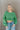 Front view of model wearing the On My Own Fringe Sweater, which features green knit fabric with fringe across the chest and sleeves, a round neckline, and long balloon sleeves. Sweater is styled tucked up.