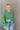 Front view of model wearing the On My Own Fringe Sweater, which features green knit fabric with fringe across the chest and sleeves, a round neckline, and long balloon sleeves. Sweater is styled tucked up.