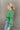 Side view of model wearing the On My Own Fringe Sweater, which features green knit fabric with fringe across the chest and sleeves, a round neckline, and long balloon sleeves. Sweater is styled tucked up.