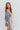 Side view of model wearing the Wonderful Life Dress in Sage, which features iridescent fabric, 3/4 balloon sleeves with buttoned cuffs, a v neck and back, and a cutout at the waist.