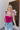 Front view of model wearing the Luna Velvet Bodysuit in Pink, which features magenta velvet fabric, satin tie straps, and a cheeky bottom. Worn with jeans.