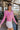 Frontal side view of model wearing the Lucky Me Sweater in Pink, which features a pink knit material, a scoop neck, long sleeves, ruffle detailing at the front sides, and a thick bottom hem