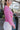 Side view of model wearing the Lucky Me Sweater in Pink, which features a pink knit material, a scoop neck, long sleeves, ruffle detailing at the front sides, and a thick bottom hem