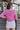 Back view of model wearing the Lucky Me Sweater in Pink, which features a pink knit material, a scoop neck, long sleeves, ruffle detailing at the front sides, and a thick bottom hem