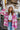 Front view of model wearing the Park City Plaid Shacket, which has a pink and white plaid pattern, a button-up front with tortoise buttons, front chest pockets and corduroy trim. Worn unbuttoned over white top