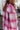 Close-up side view of model wearing the Park City Plaid Shacket, which has a pink and white plaid pattern, a button-up front with tortoise buttons, front chest pockets and corduroy trim. 