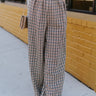 Front view of model wearing the New In Town Tweed Pants, which feature brown and black tweed fabric, a paperbag waist, a matching belt with a gold buckle, and wide legs.