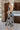 Full body side view of model wearing the It's Fate Floral Midi Dress, that has black satin fabric with a blue, white, and cream floral print, bustier cups with wiring, criss-cross straps that tie in the back, and a side slit.