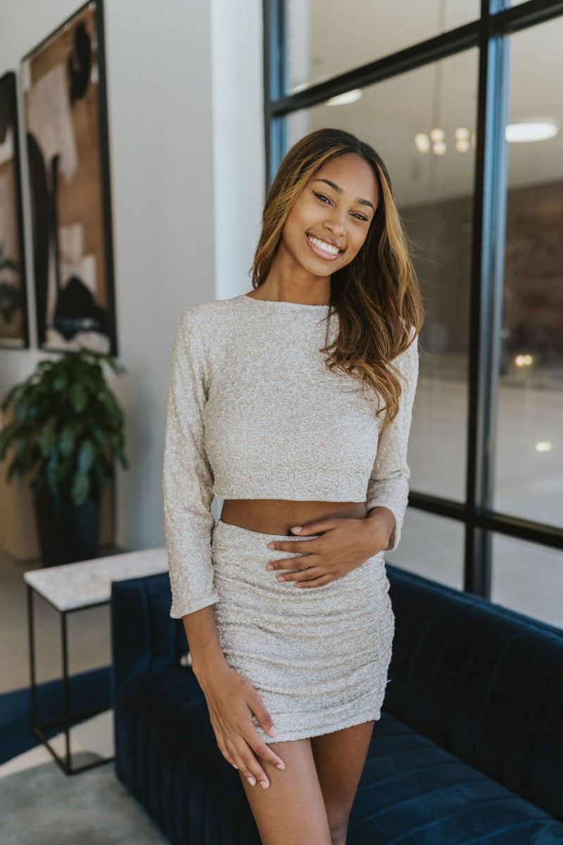 Front view of model wearing the Shine On Sequin Skirt in Champagne, that has beige mesh material with beige sequins, a beige lining, 3/4-length sleeves with shoulder pads, and an exposed back zipper.