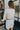 Back view of model wearing the Shine On Sequin Top in Champagne, that has beige mesh material with beige sequins, a beige lining, 3/4-length sleeves with shoulder pads, and an exposed back zipper