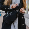 Close front view of model wearing the Easy Going Sling Bag that features black fabric, adjustable cross over straps, and two pockets with zipper closures.