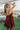 Side view of The Holiday Plans Dress features burgundy sheen fabric, babydoll style, square neckline with adjustable spaghetti straps, mini length and a bow on the back.