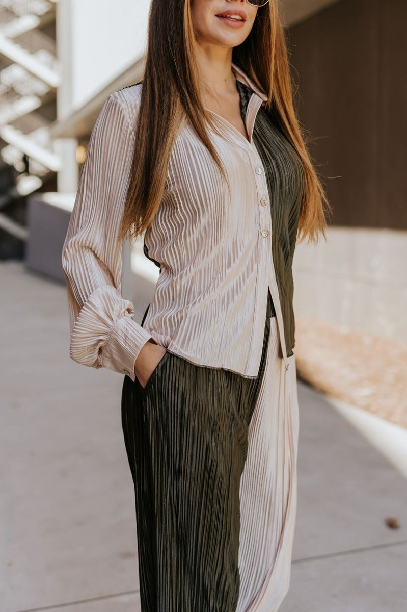 Close side view of model wearing the Block It Out Pants that have olive and cream color block coloring, plisse fabric, two front pockets, and elastic waistband, and flare wide legs with lettuce hems.