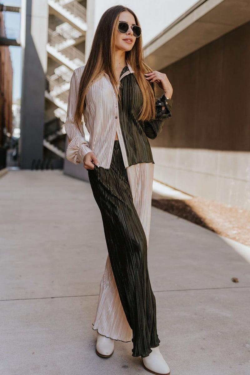 Full body front view of model wearing the Block It Out Pants that have olive and cream color block coloring, plisse fabric, two front pockets, and elastic waistband, and flare wide legs with lettuce hems.